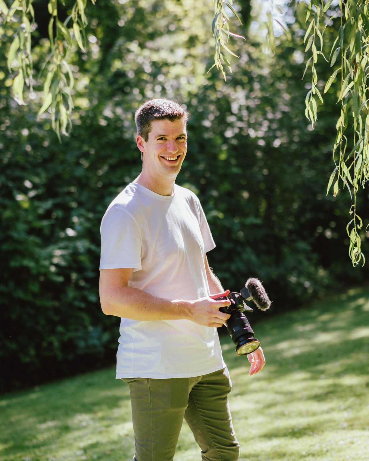 Le photographe souriant tient son appareil, sous les branches d'un saule