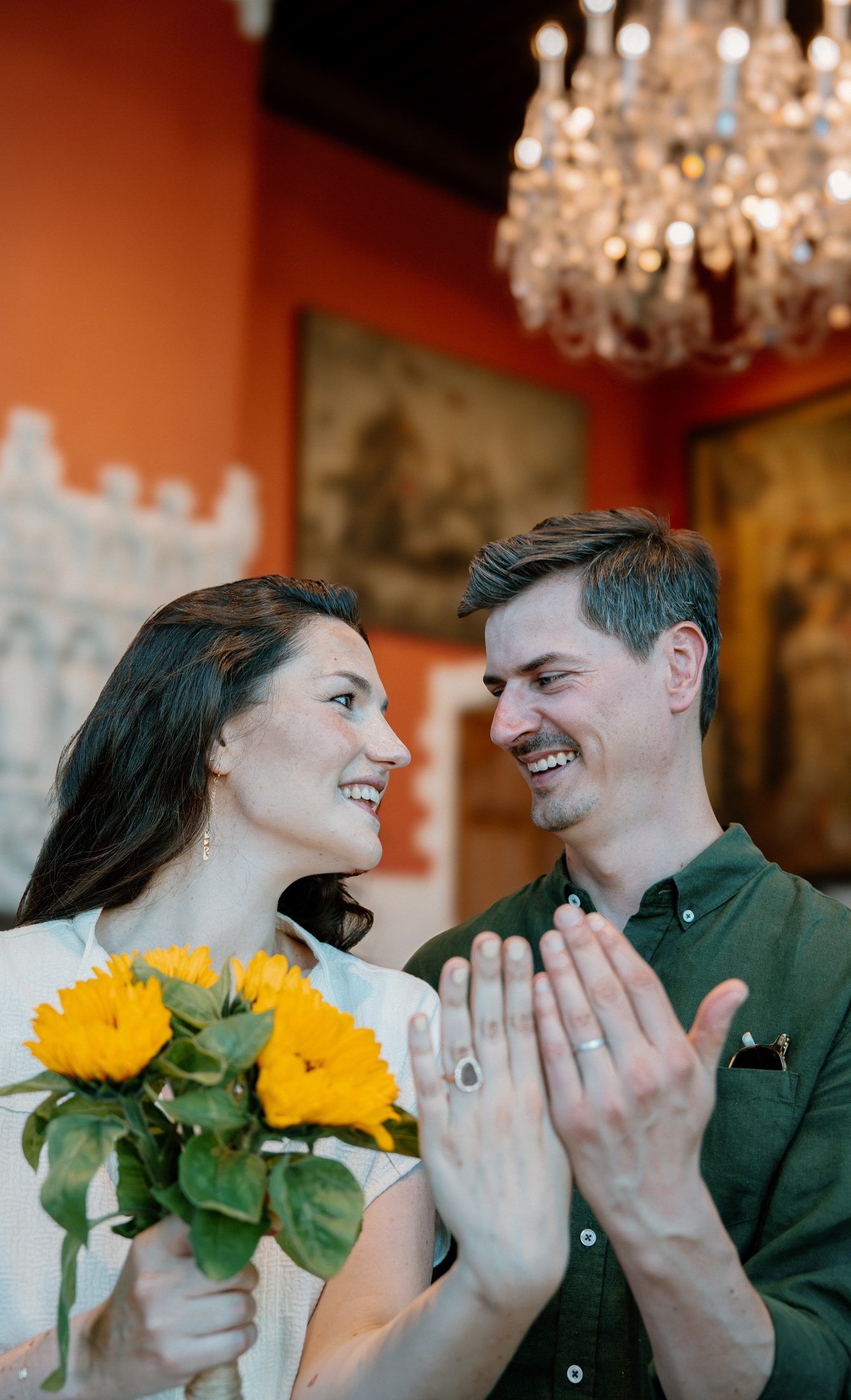 Le couple rit en montrant ses alliances, lustre en cristal et murs orangés