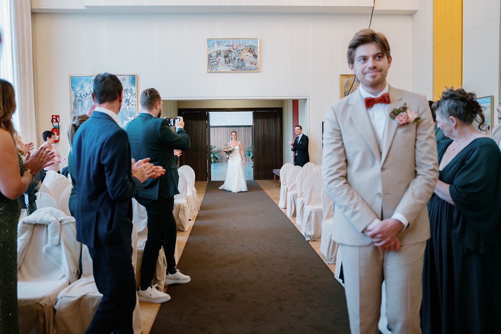 Le marié se retourne en souriant vers la mariée qui remonte l'allée