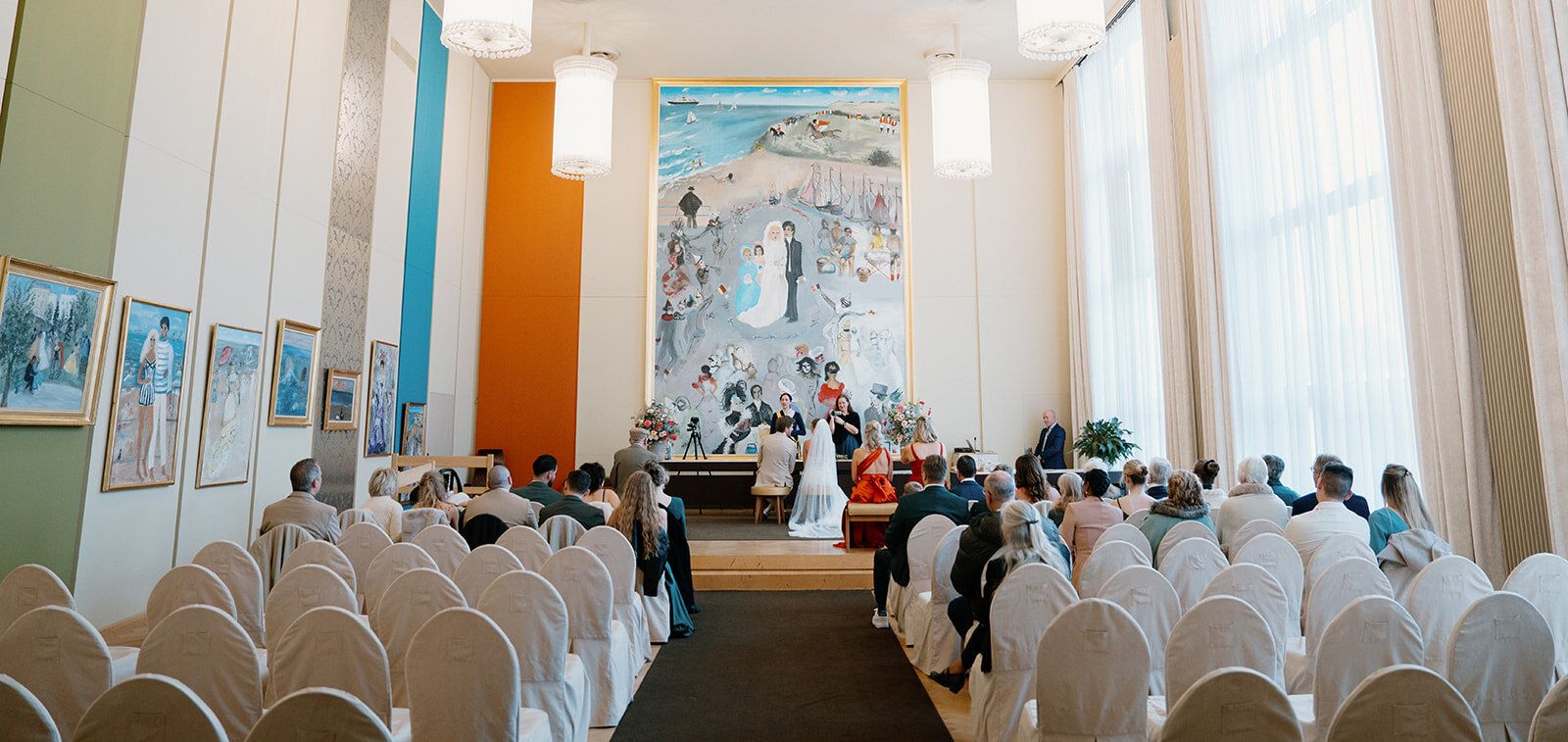 Vue d'ensemble de la salle de cérémonie, invités assis face à une fresque murale