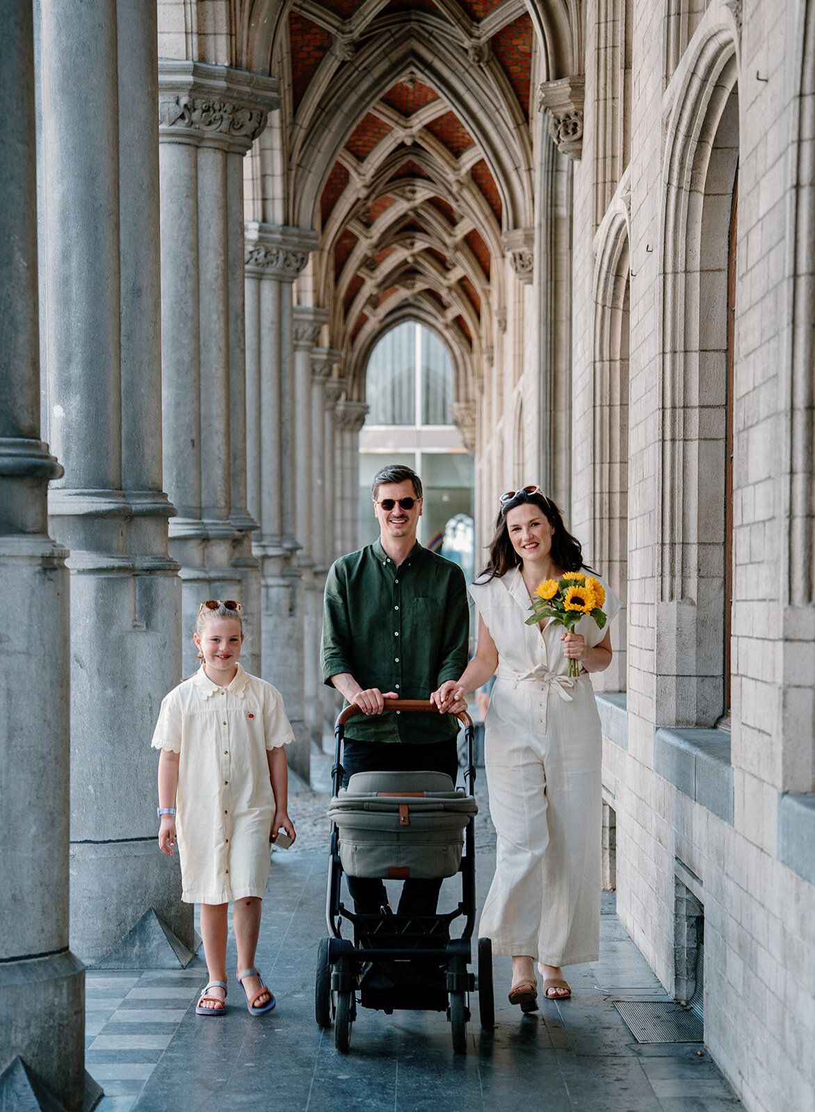 La famille marche sous une arcade gothique, poussette et bouquet de tournesols