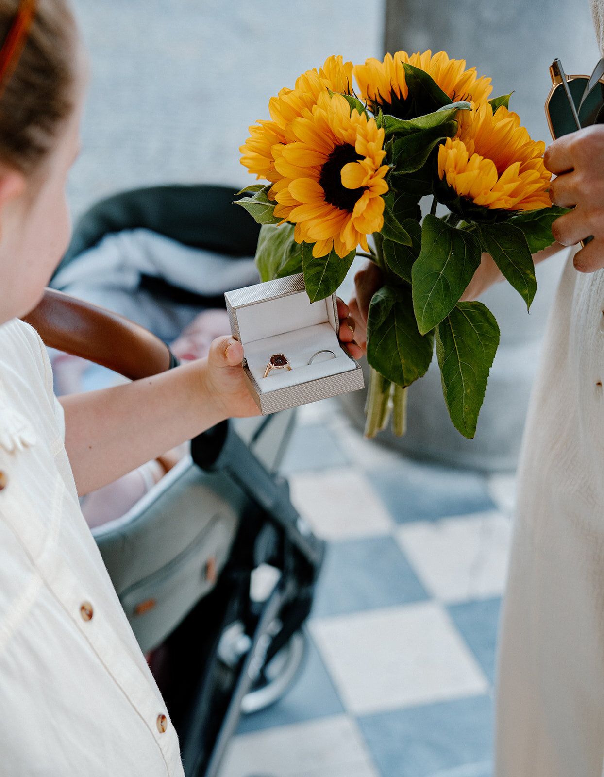 Une fillette tend un écrin à bague, bouquet de tournesols à côté