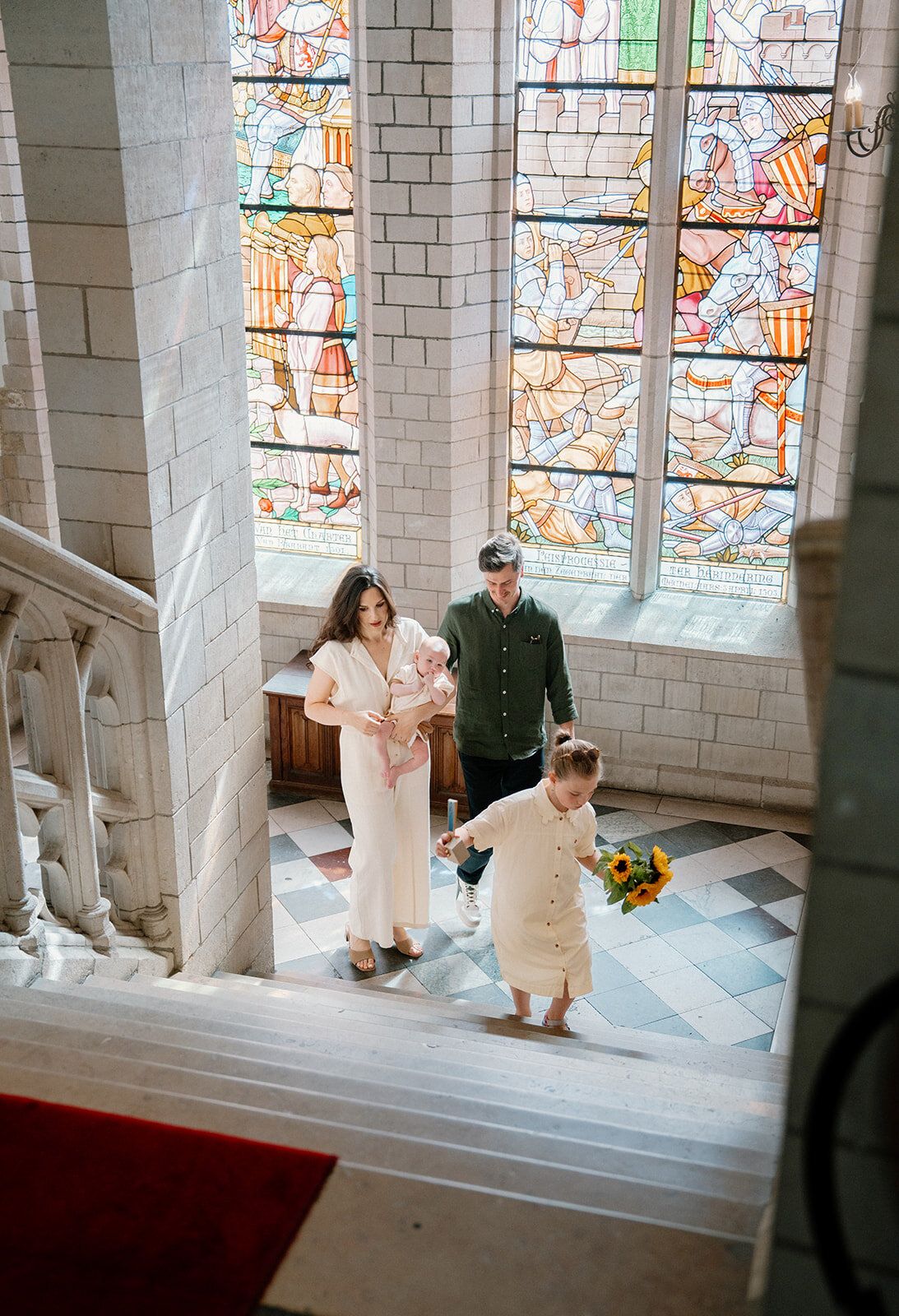La famille descend un escalier, vue plongeante sur des vitraux colorés