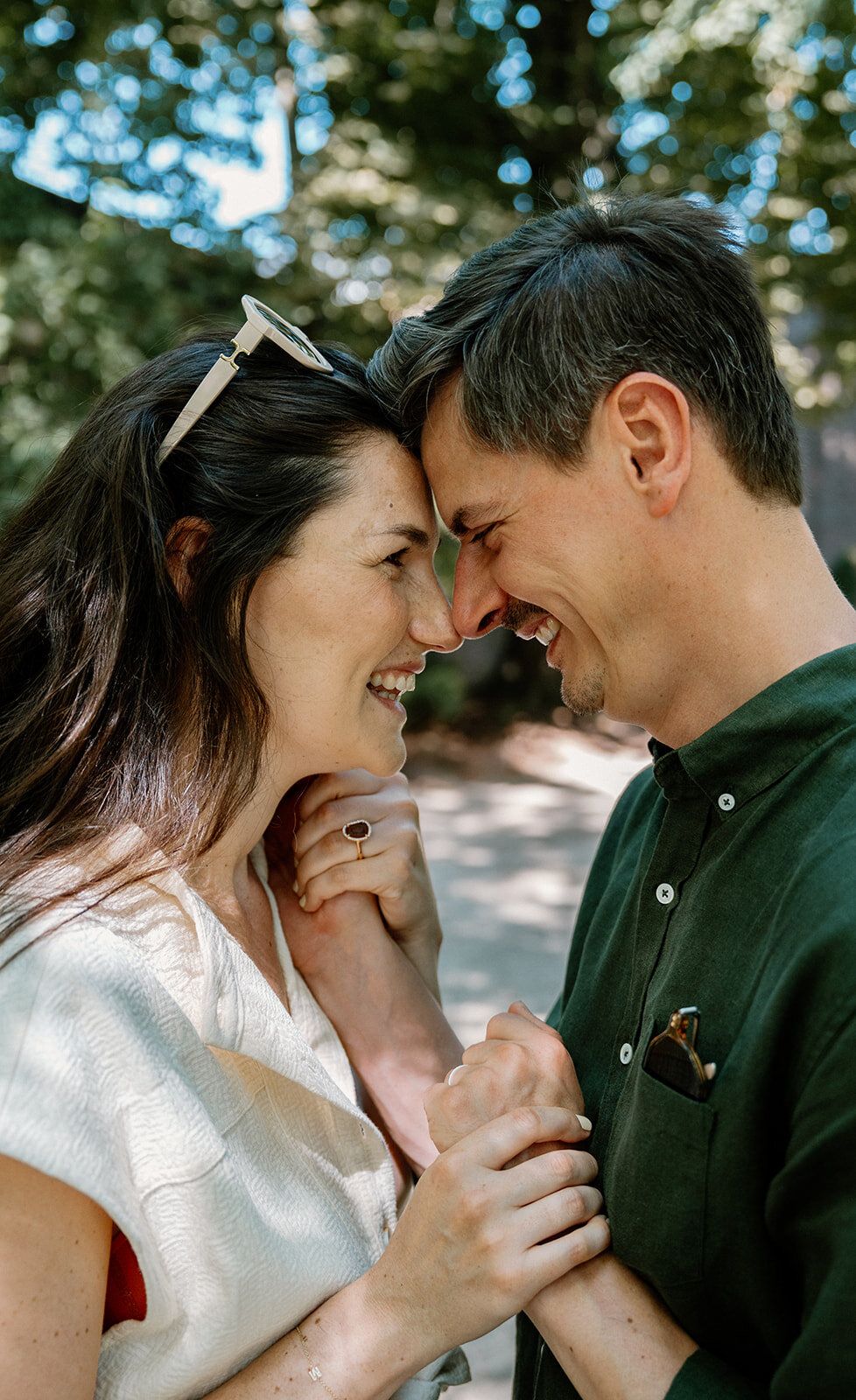 Front contre front, le couple sourit sous les arbres en pleine lumière